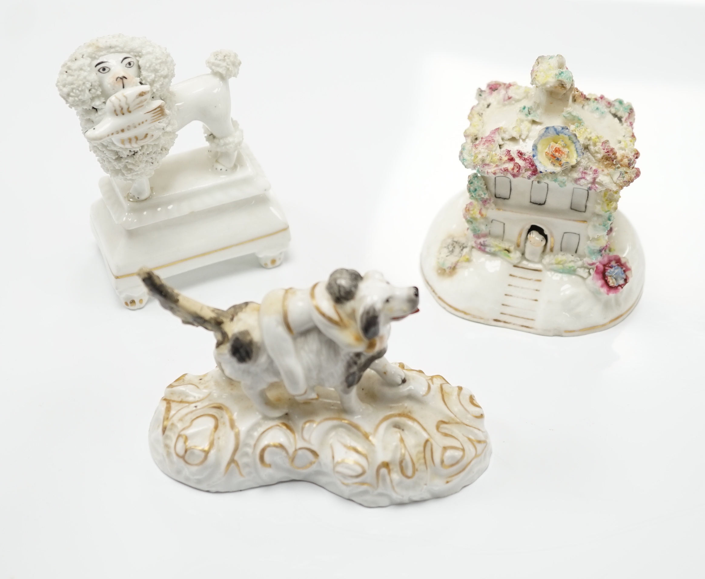 Three Staffordshire porcelain dog figures, c.1830-50, comprising a boy clinging to the back of a spaniel, a model of a poodle with a bird in its mouth and a model of a cottage with a small dog in the doorway, tallest 9cm